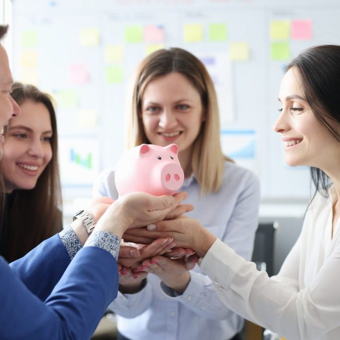 Group,of,people,holding,pink,piggy,bank,in,office